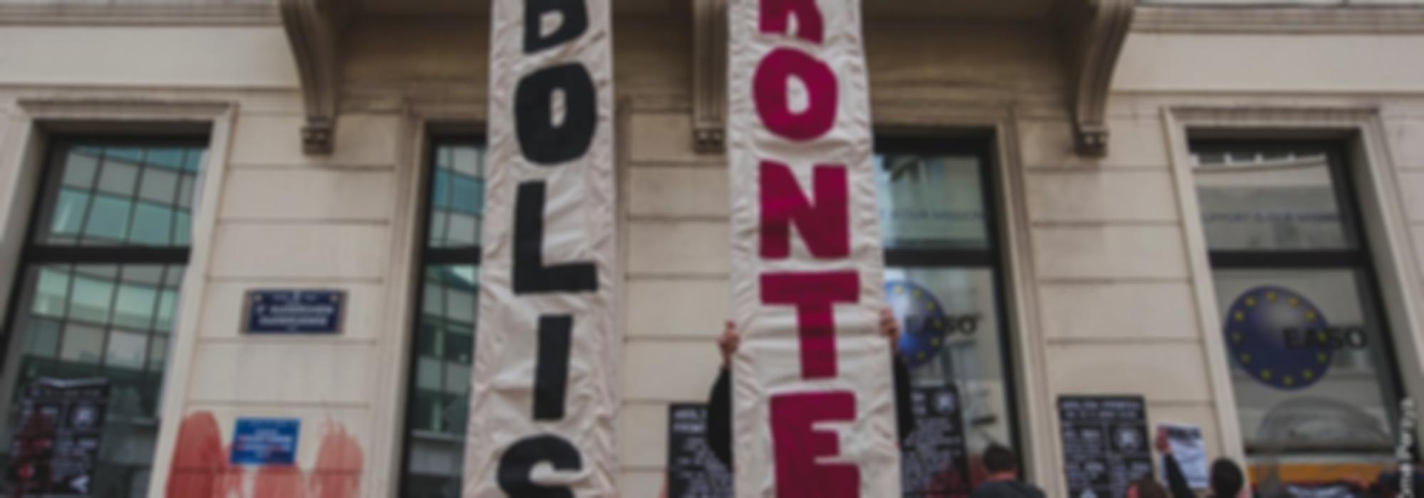 foto van actie bij frontex kantoor in brussel. 2 mensen houden 2 verticale banners op waarop "Abolish" "Frontex" staat.