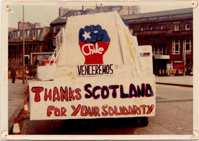 je ziet een paradewagen met daarop een gebalde vuist en "Thanks Scotland for your solidarity"