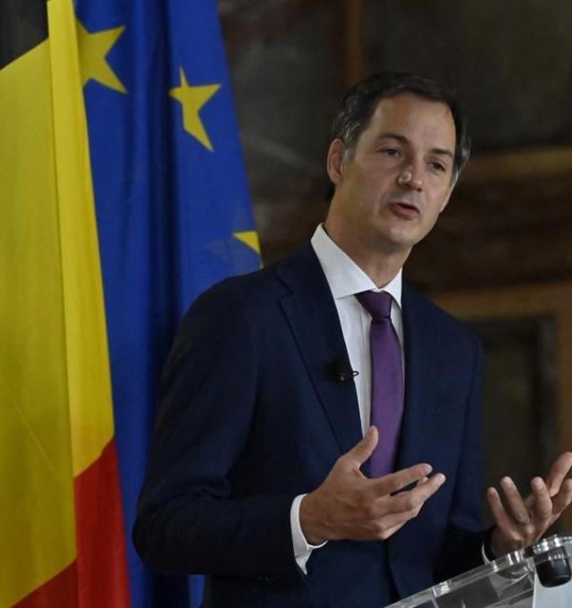 Alexander De Croo houdt een toespraak, achter hem zie je de vlaggen van België en van de EU.